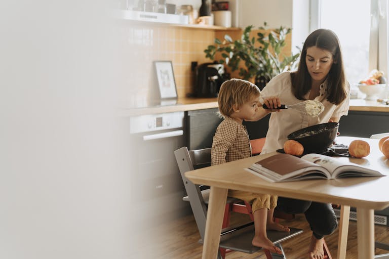 A mom and her child baking in a cozy kitchen surrounded by pumpkins.
